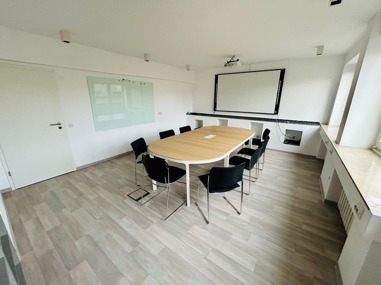 Besprechungsraum mit ovalem Tisch für zehn Personen, Leinwand und Whiteboard